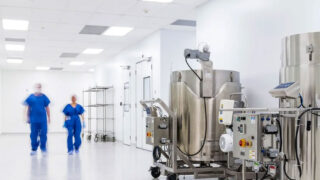 Two persons walking in a bright hallway of cell and gene therapy production facility.