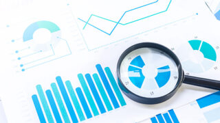 A magnifying glass on a paper with blue charts.